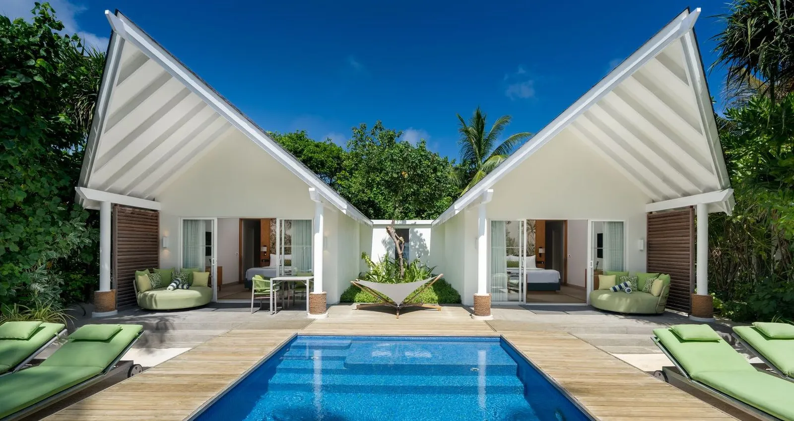 The 2 white wings of a 2BR Family Beach Villa with Pool around the pool, with green loungers.