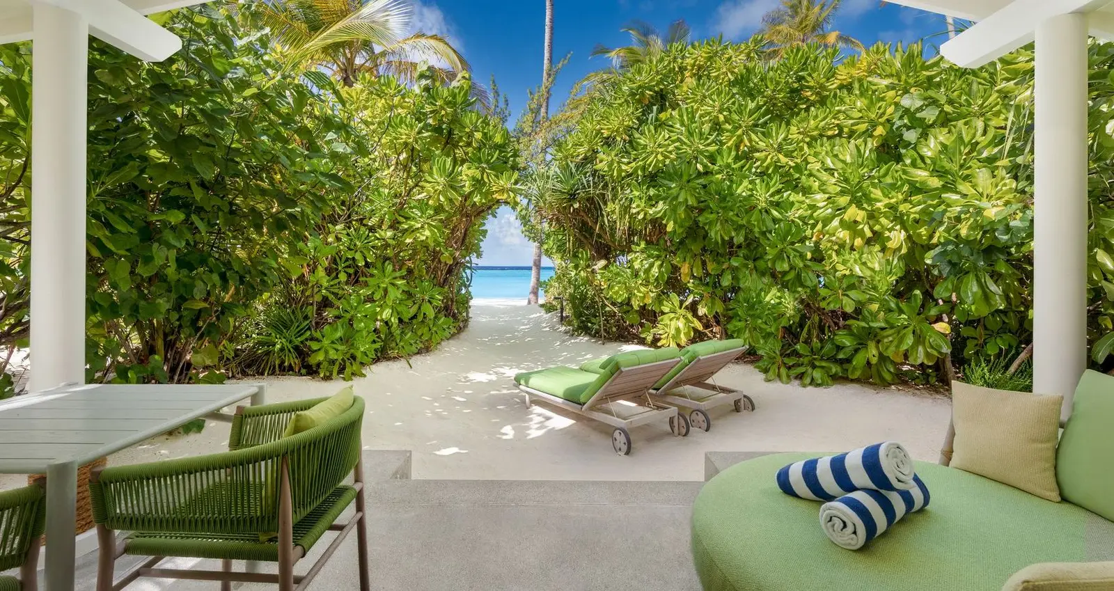 A Beach Villa’s terrace, with the green daybed, the table and the path to the beach through the bushes.