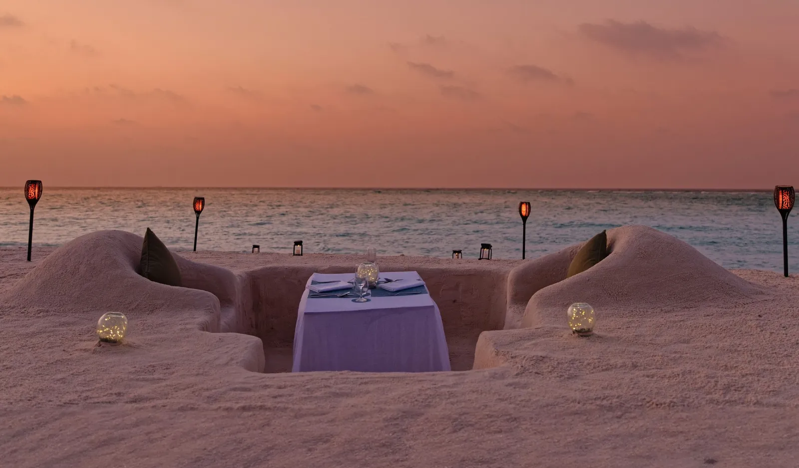 The Veli dinner at sunset: a table laid in a hollow dug into the sand, with torches along the shore.
