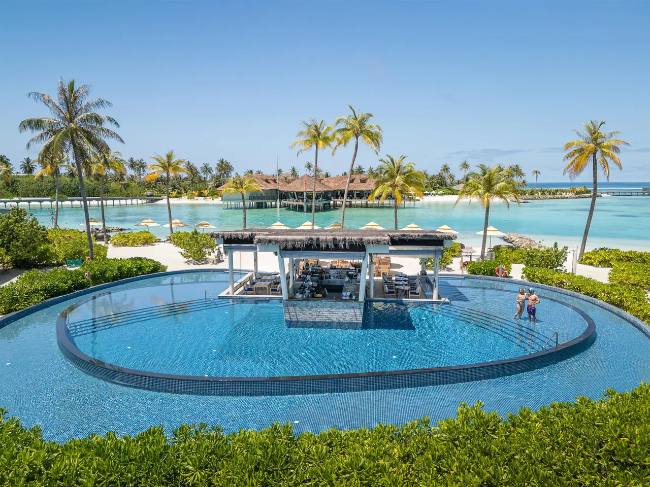 The round pool with its bar in the middle, among the palms, with the lagoon and overwater villas behind.