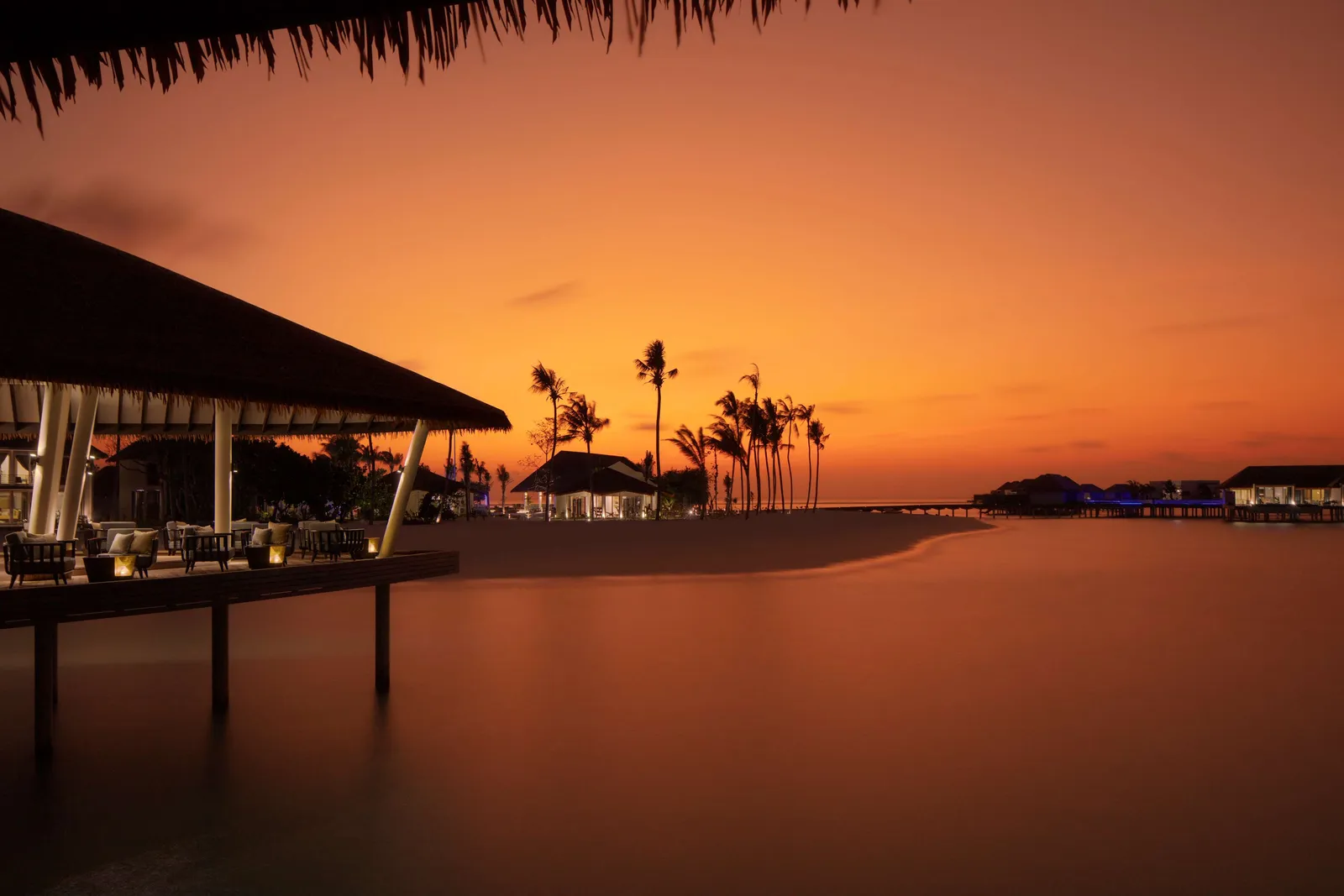 Mahurab at sunset, the overwater bar under its sloping roof, with palms in silhouette.