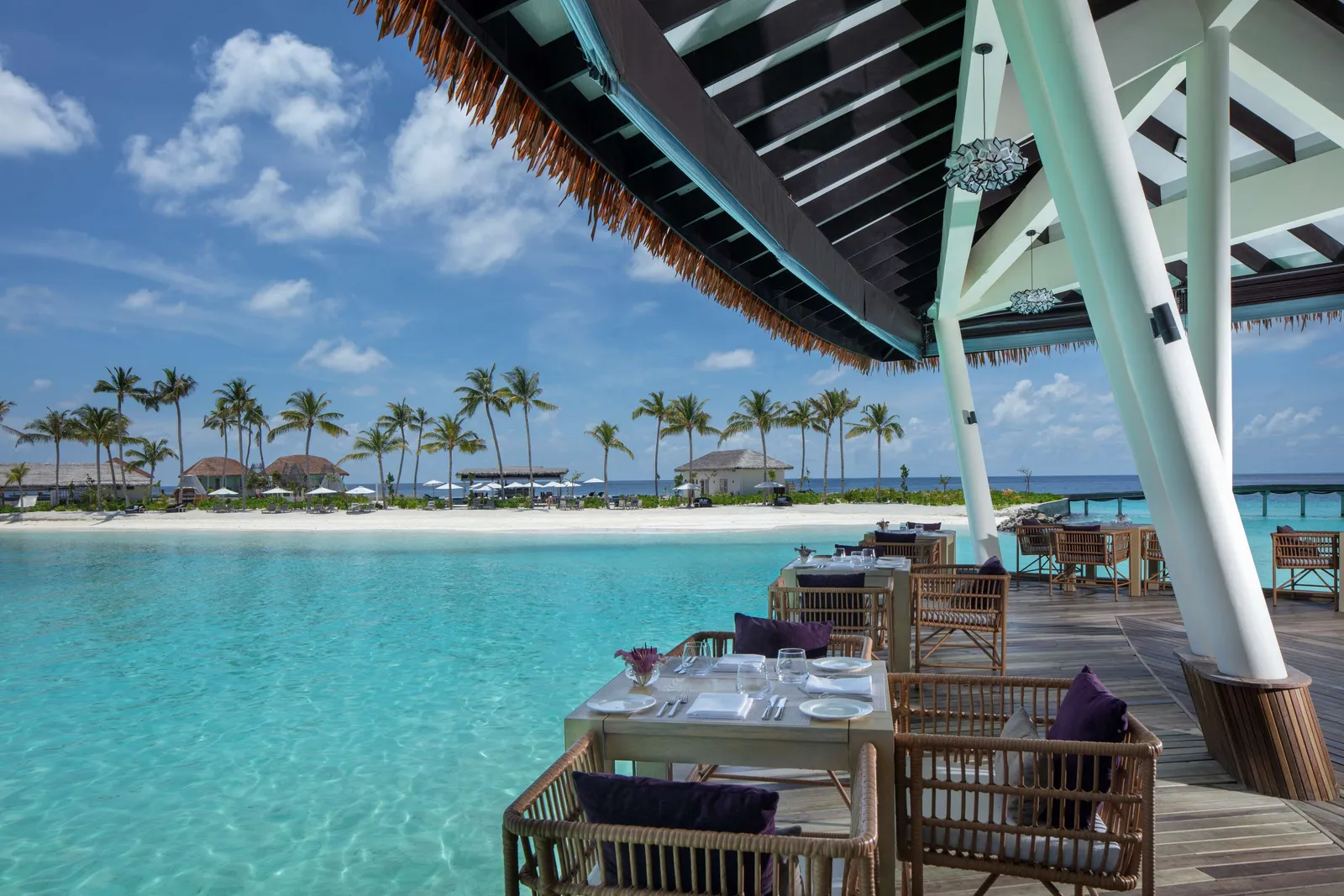 Raha’s tables on the timber deck over the lagoon, under the awning, facing the beach and the palms.