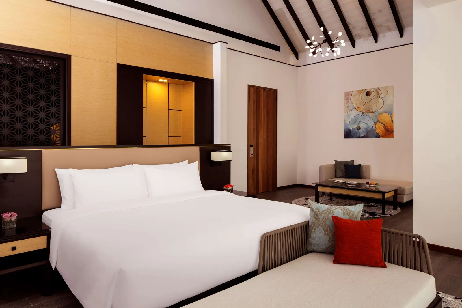 An overwater villa bedroom, with its king bed, red cushions and pitched timber ceiling.