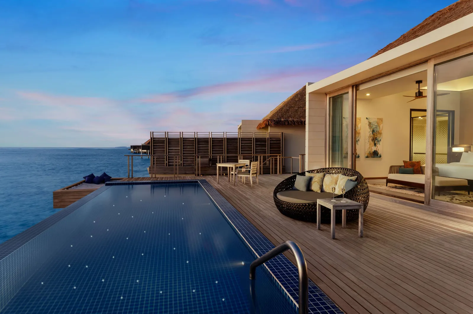 An overwater villa’s private pool at dusk, a round daybed on the deck and the sea all round.