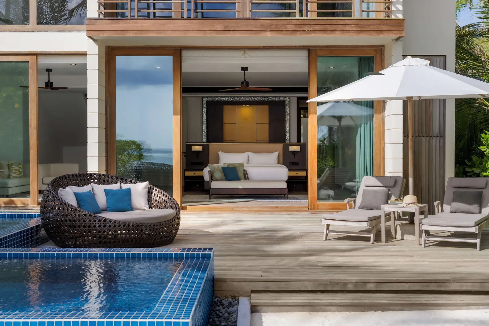 The deck of a 2-bedroom family villa, with its pool, round daybed, loungers and the bedroom open behind.