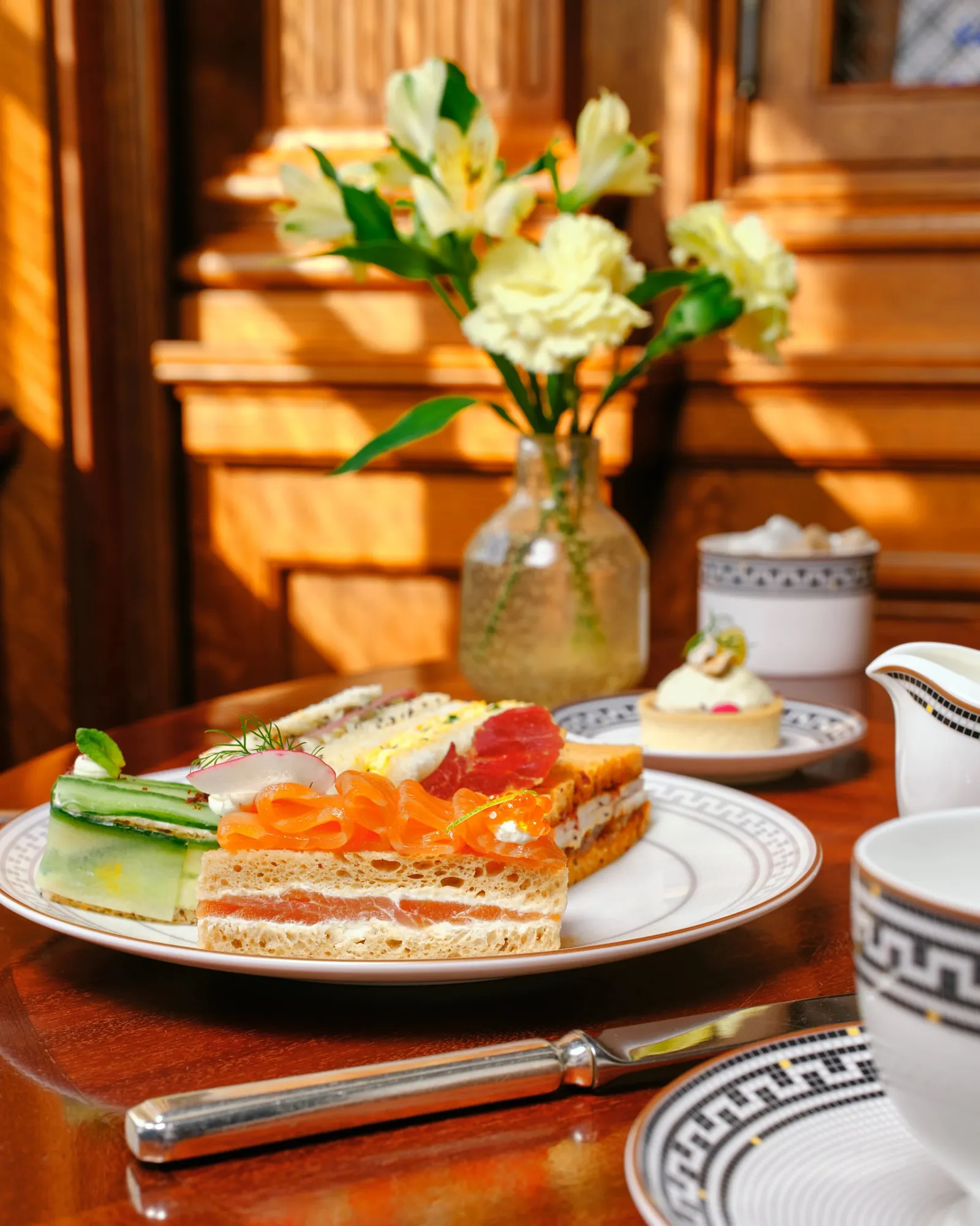 Tea in The Drawing Room: a salmon sandwich, white flowers and a vase on a wooden table