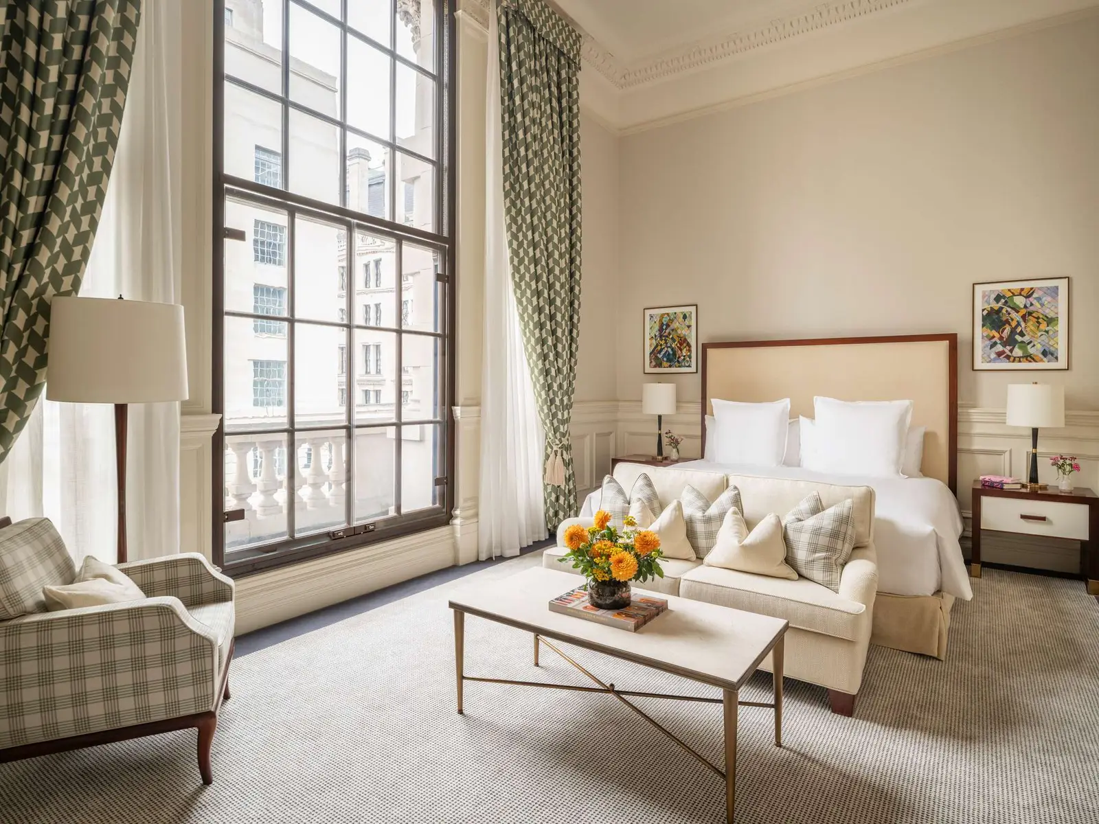 An Executive room: a white bed, a low table with yellow flowers and a sofa before the windows