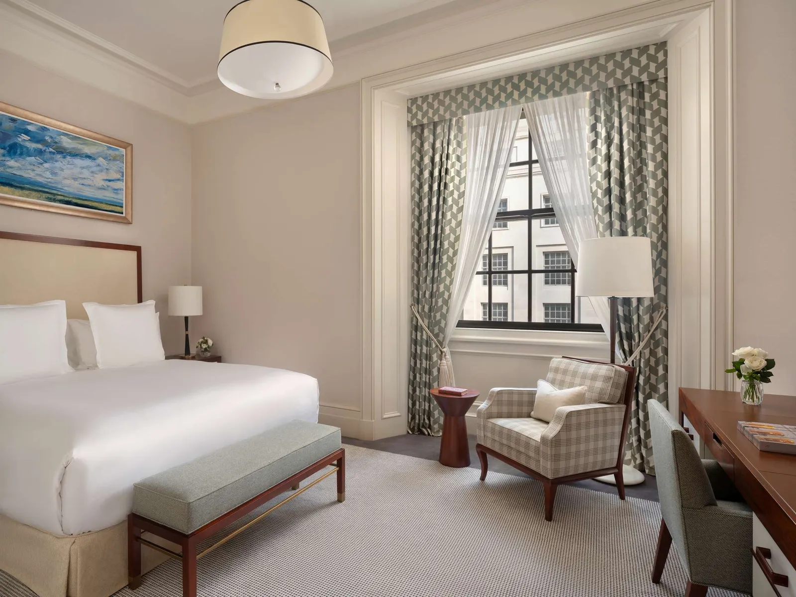 A Superior room: a white bed with a bench at its foot, pictures on the walls and a window with check curtains