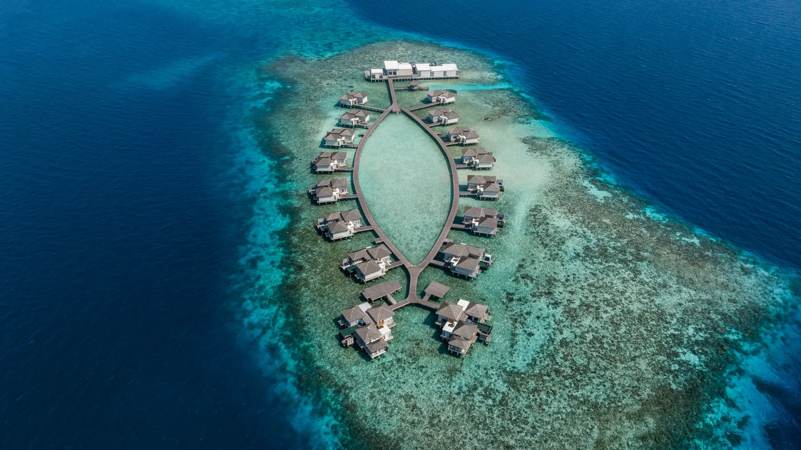 The overwater island from above, its villas set in a teardrop on the edge of the reef