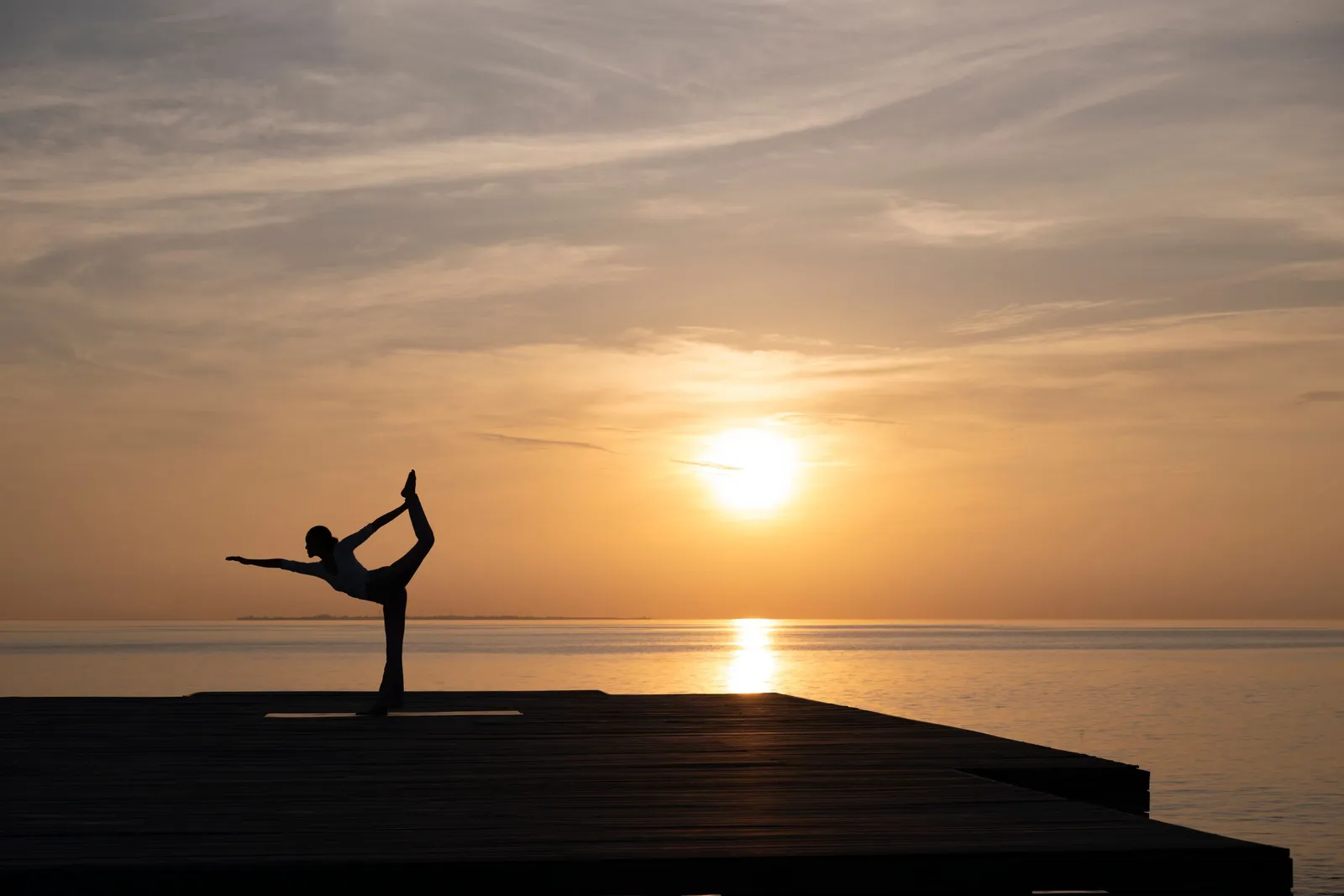 A woman in a yoga pose on the deck, against the sunset