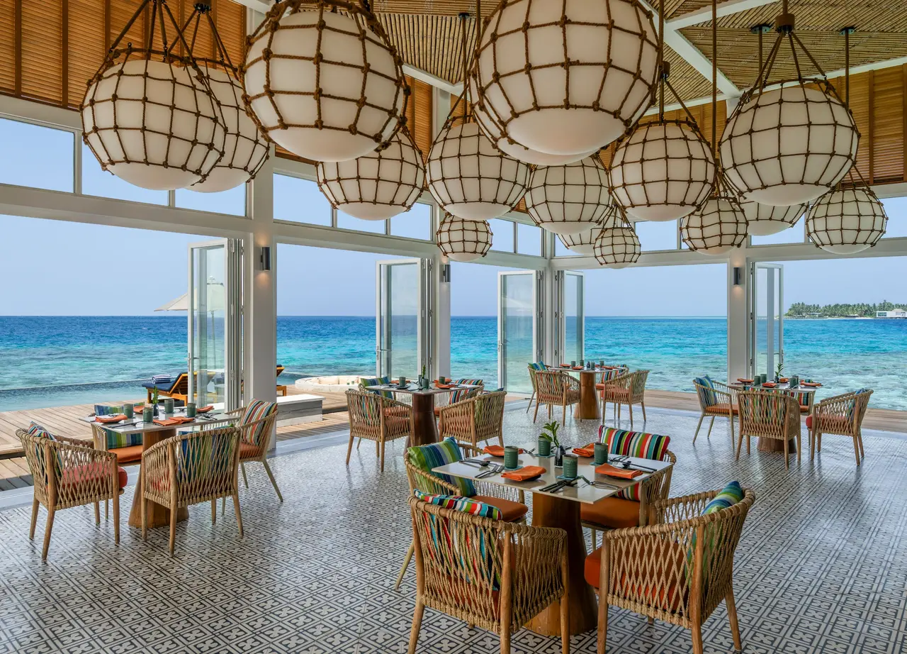 Yuzu’s overwater dining room, wicker lamps above the tables and the lagoon beyond the glass