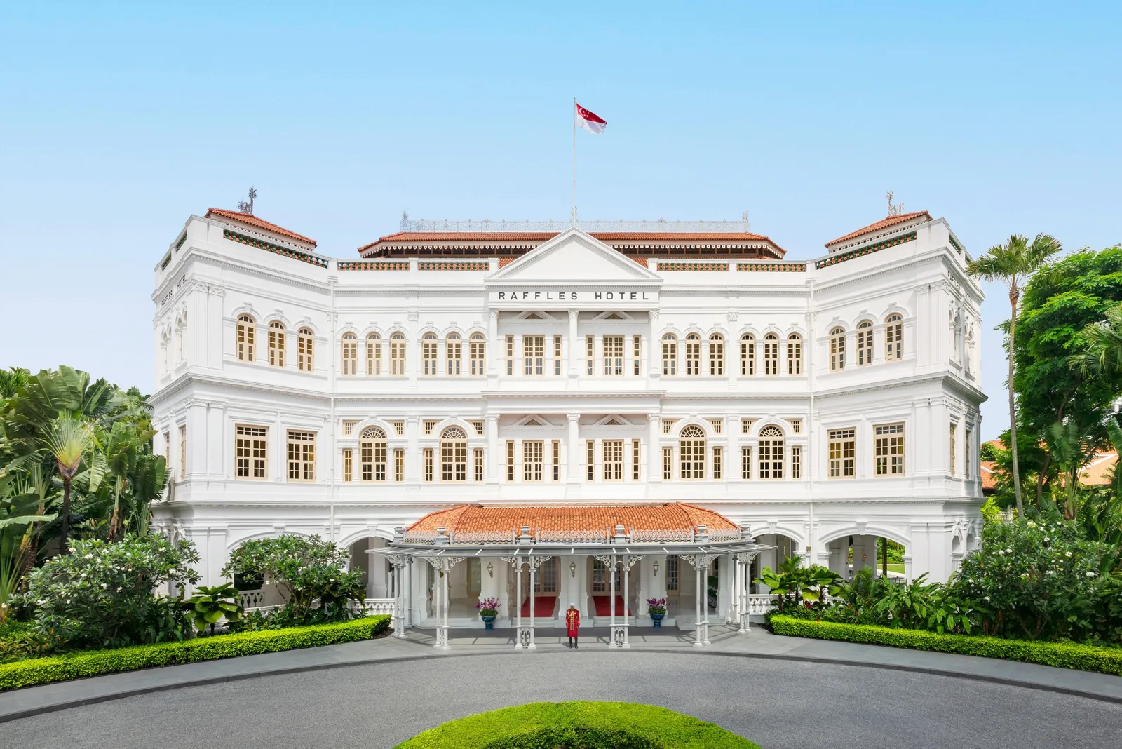 The Raffles façade by day, with Singapore’s flag on the roof and the red-and-white porch over the entrance.