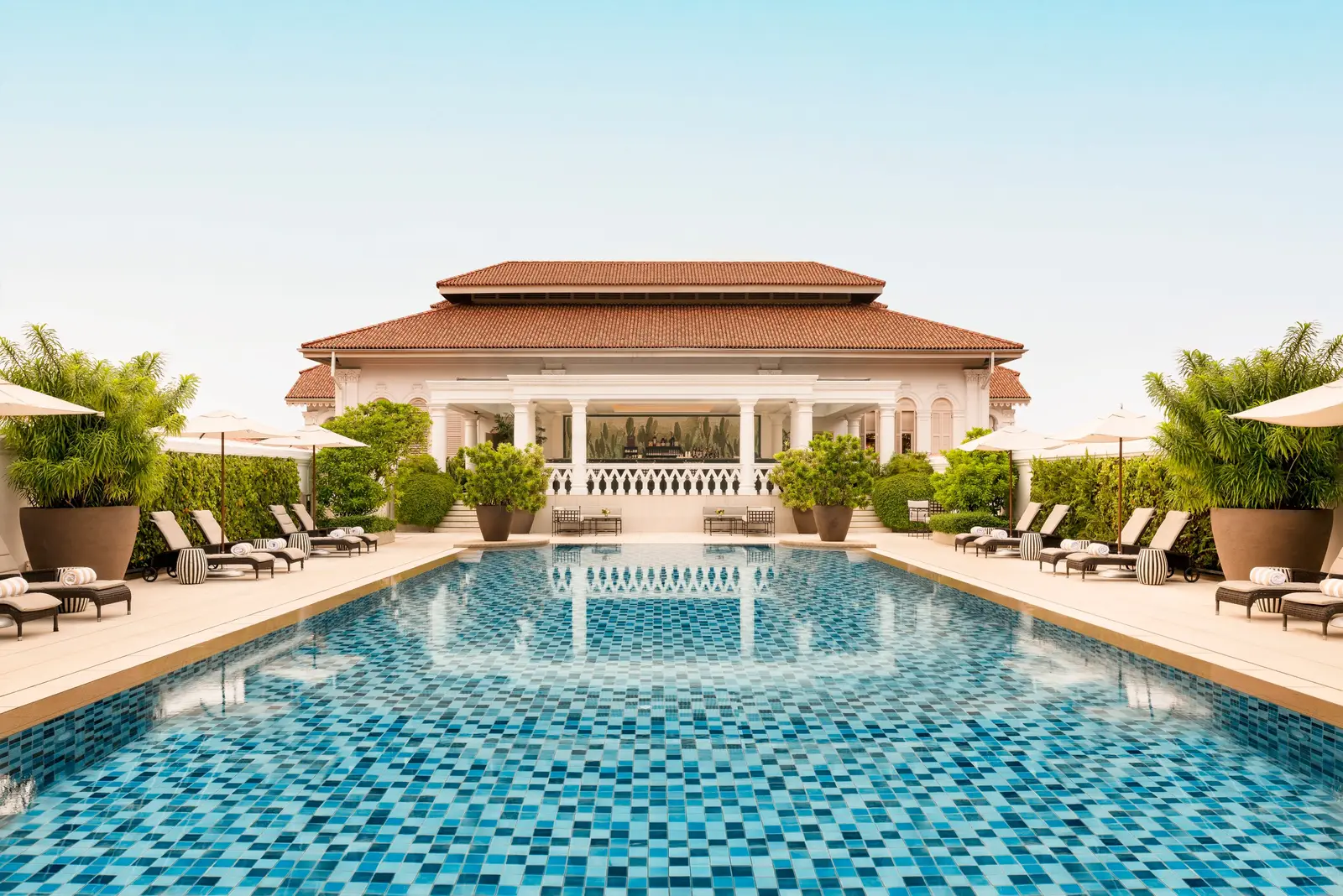 The outdoor pool lined in blue mosaic, with loungers along both sides and the tile-roofed pavilion at the far end.