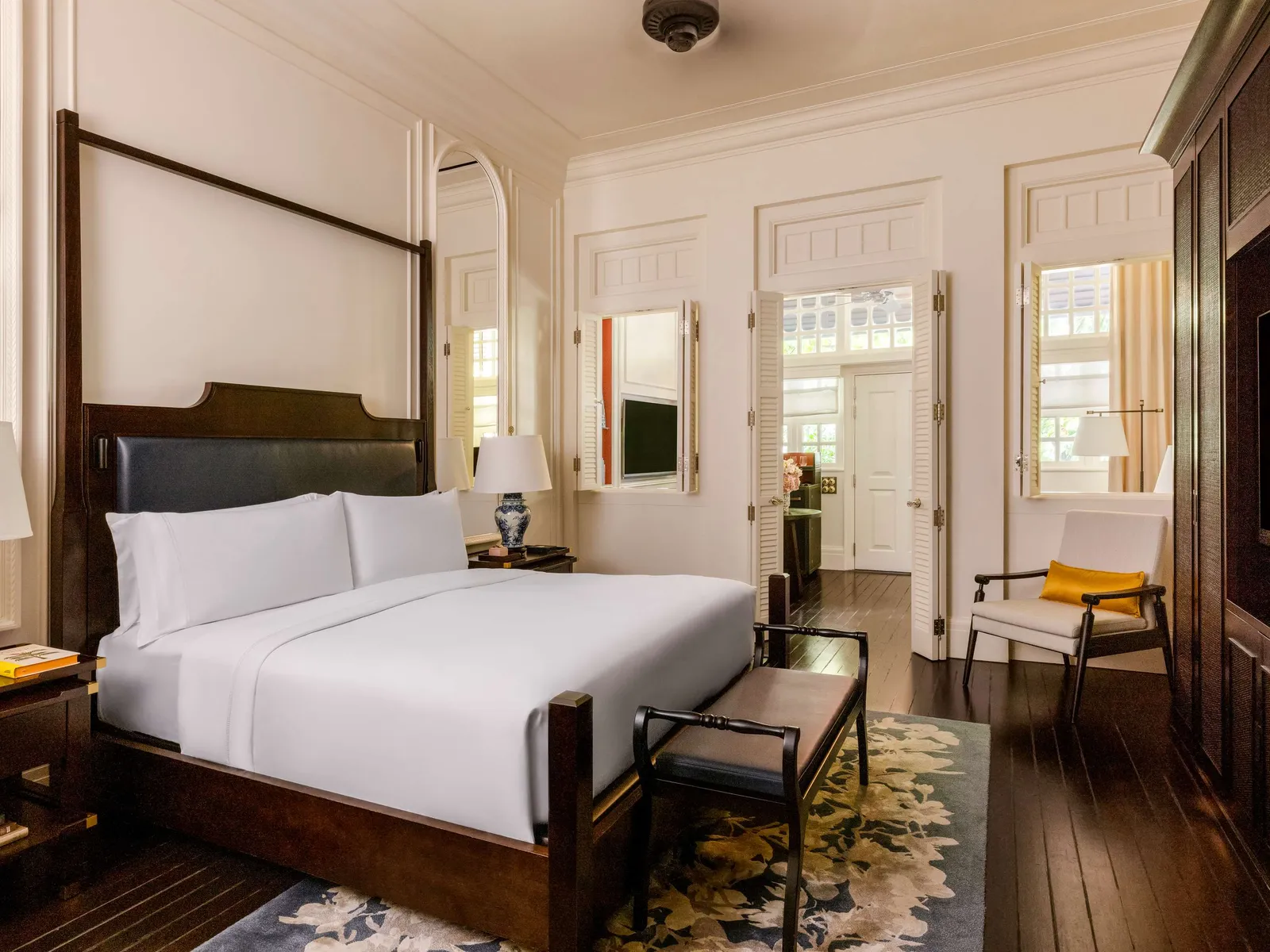 A Courtyard Suite bedroom: the dark-wood king bed, a rug of blue flowers and windows with white shutters.