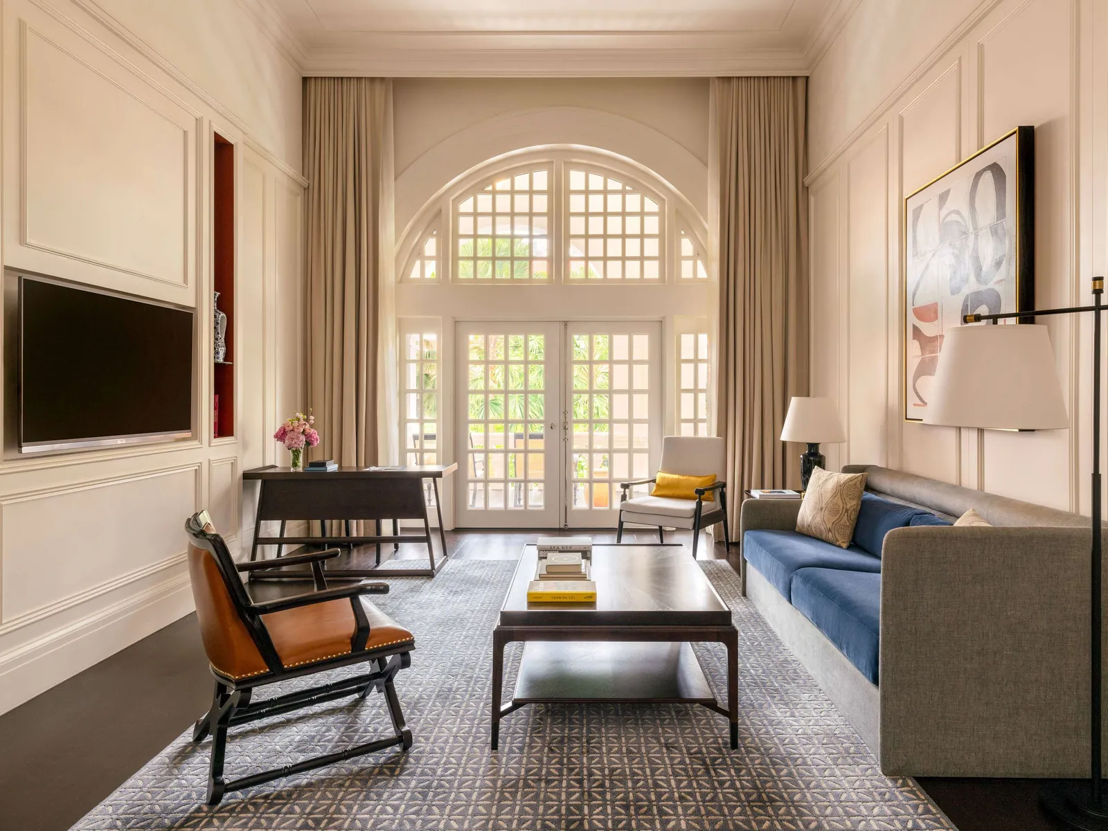 A Grand Hotel Suite’s living room: a blue sofa, a leather armchair and the arched window onto the balcony.