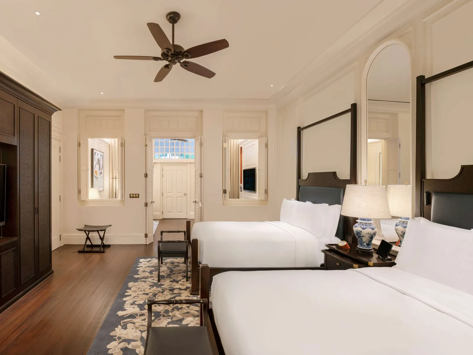 A Palm Court Suite bedroom with 2 double beds, the dark wardrobe and 3 windows at the far end.