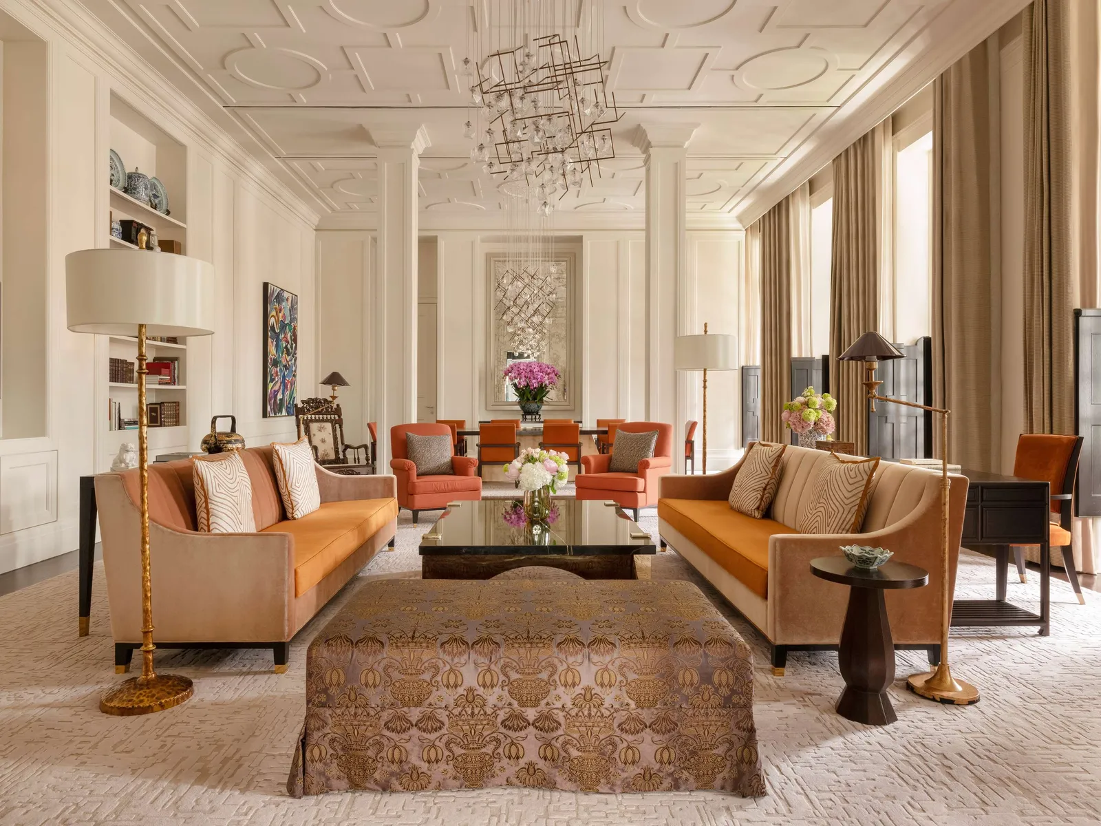 A Presidential Suite’s drawing room: 2 orange sofas, the upholstered ottoman at the centre and white columns.