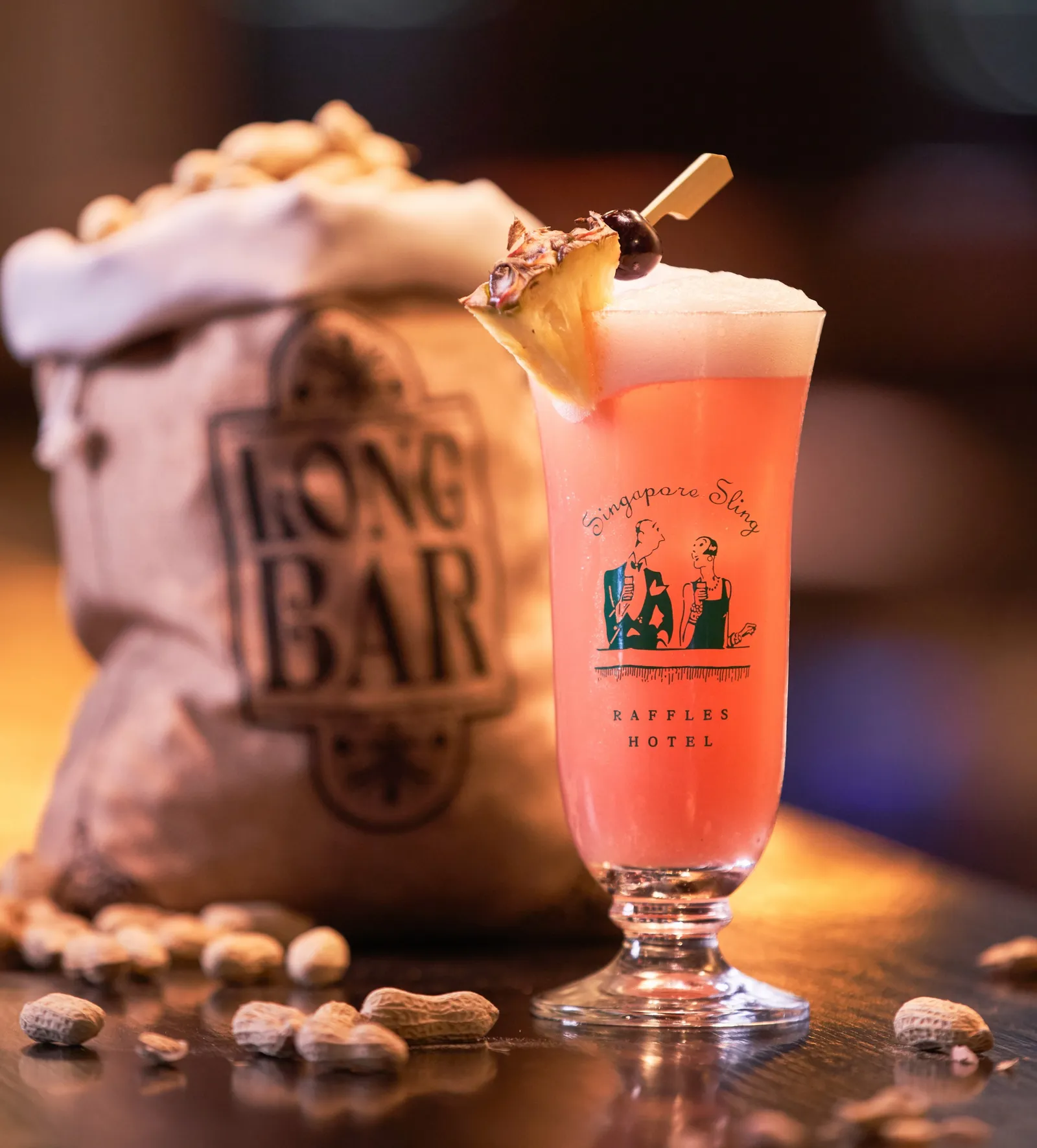 A pink Singapore Sling with its slice of pineapple, beside the jute sack of peanuts stamped Long Bar.