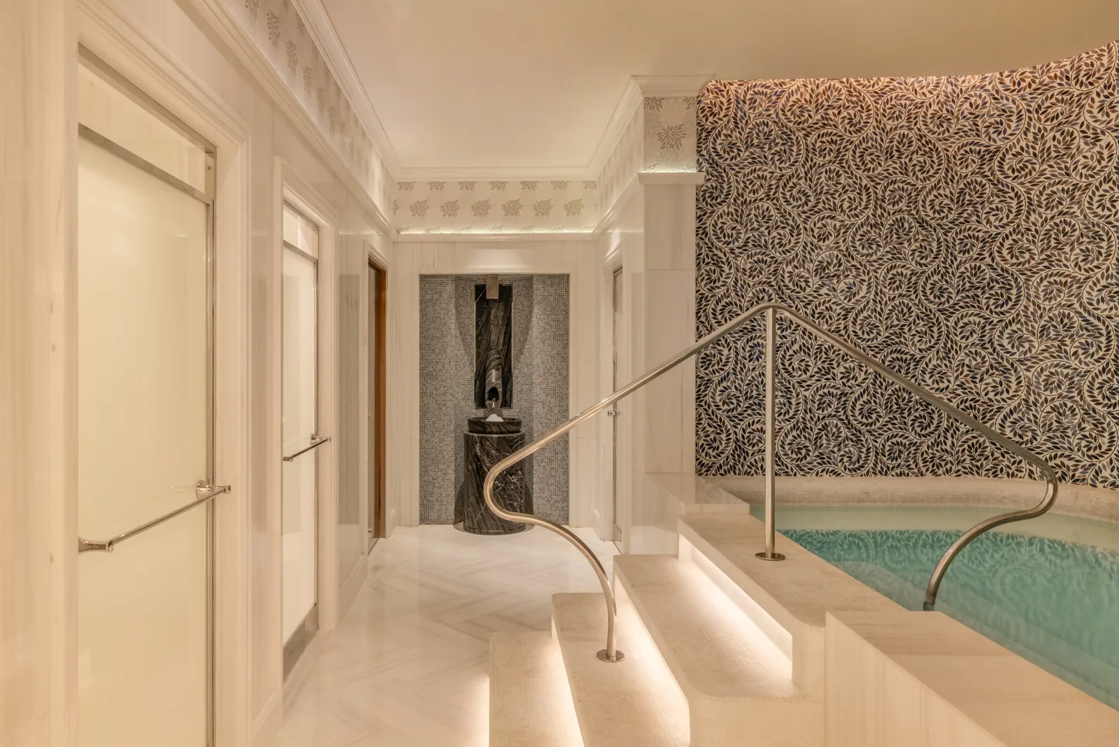 The spa’s warm pool: pale marble steps, a steel handrail and a wall of dark patterned mosaic.