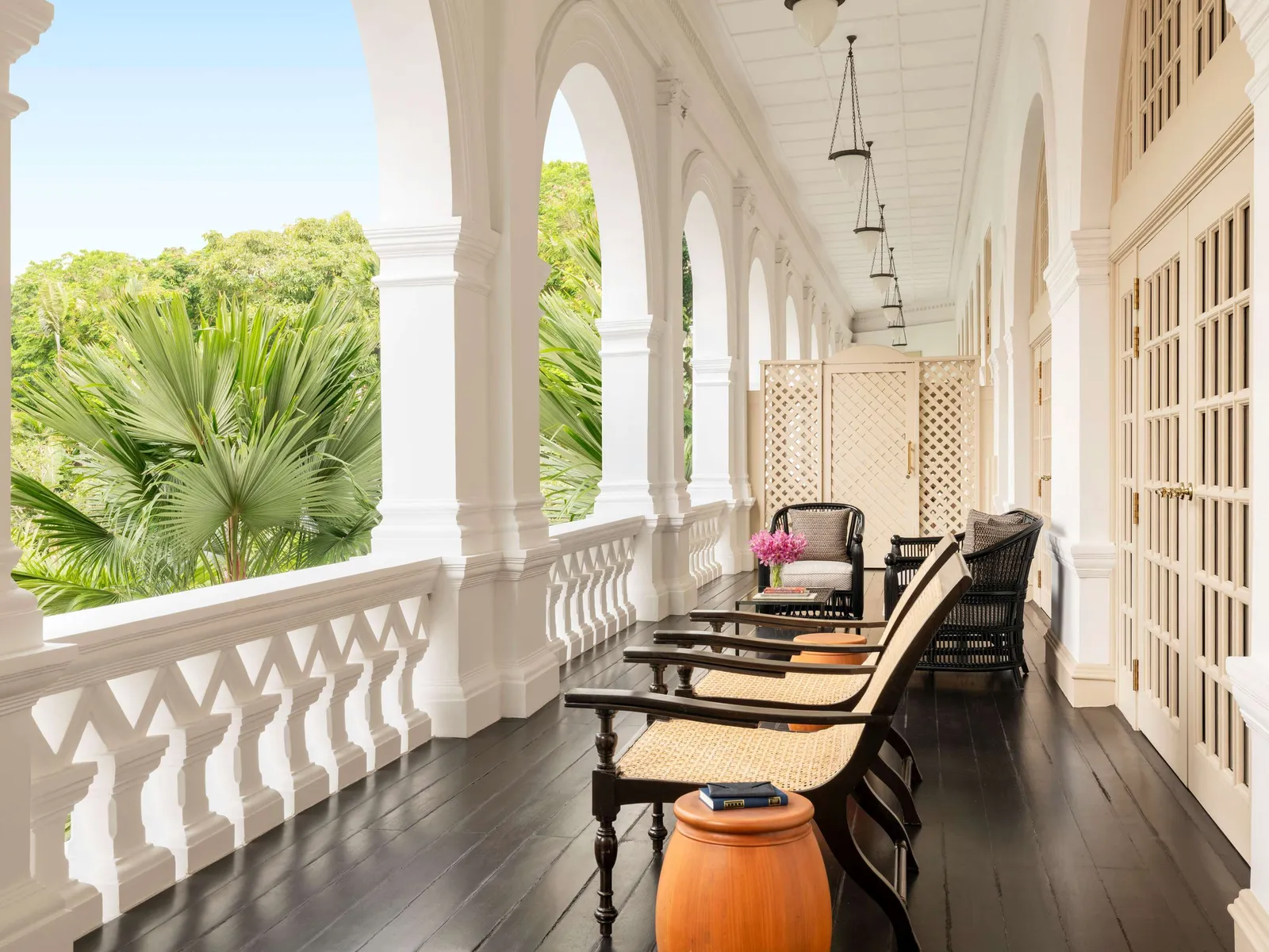 A Grand Hotel Suite’s private balcony: timber-and-cane reclining chairs under the arches, above the tops of the palms.