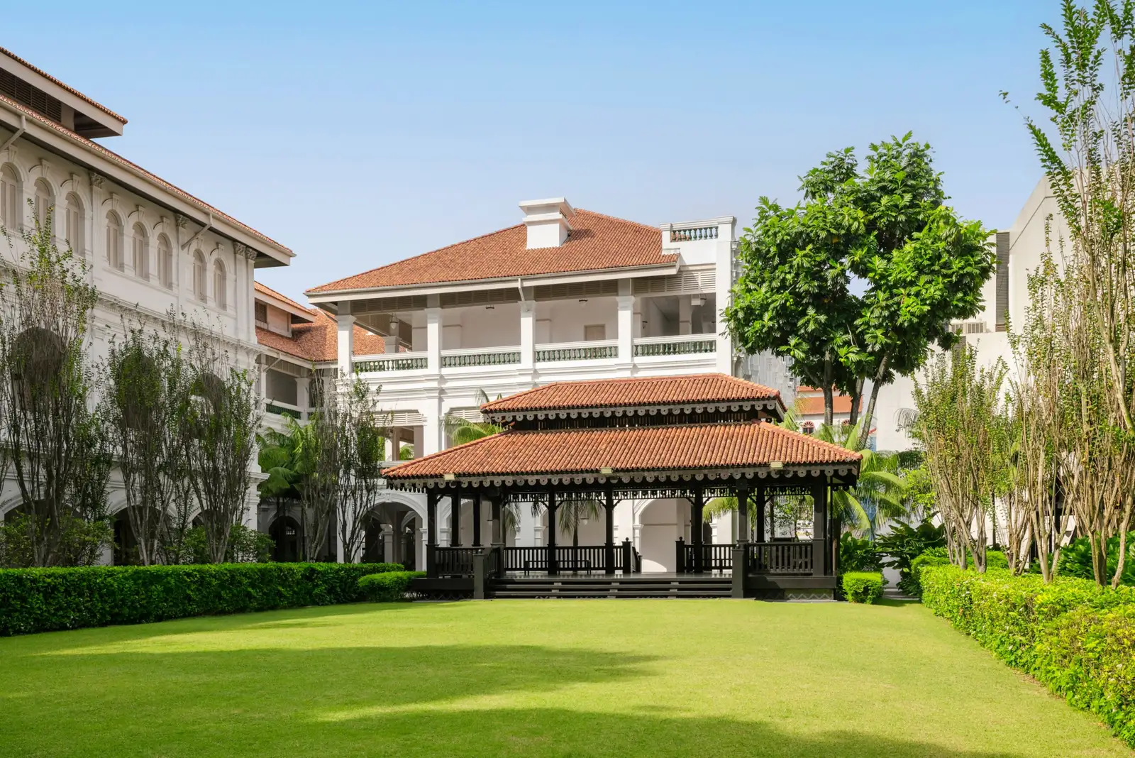 The Lawn: grass between hedges, the dark-timber pavilion with its tiled roof and the hotel’s white wings.