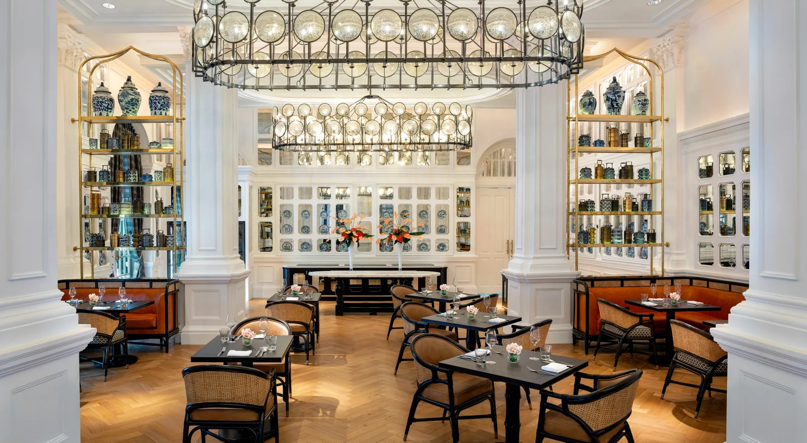 Tiffin Room: dark tables and cane chairs between white columns, shelves of blue-and-white porcelain and a ring chandelier of glass globes.