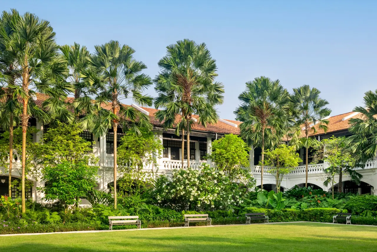 The lawn and palms of the Palm Court, with 2 floors of verandahs under red-tiled roofs.