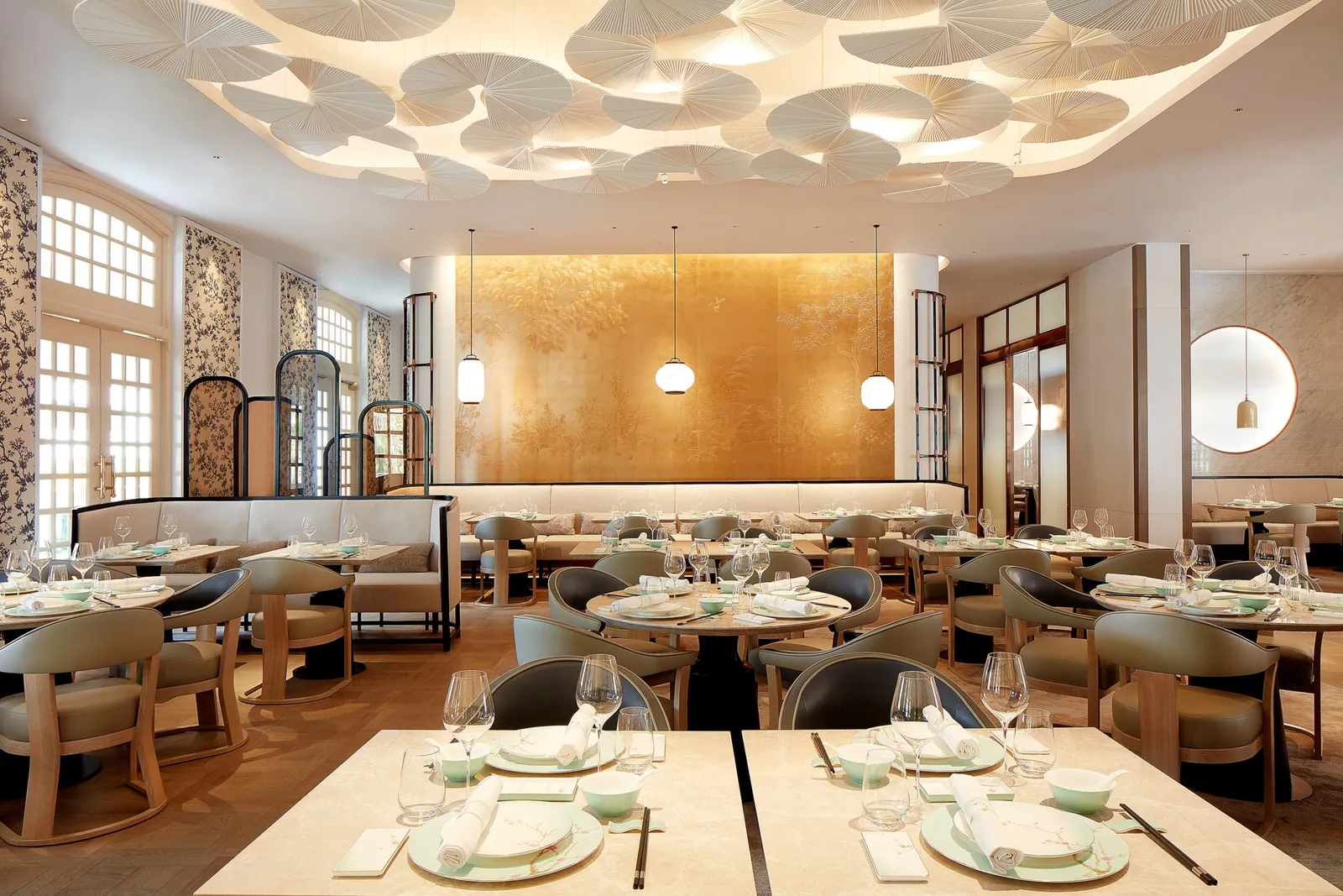 The dining room of yì by Jereme Leung: tables set with pale-green porcelain under a ceiling of white sculpted leaves.