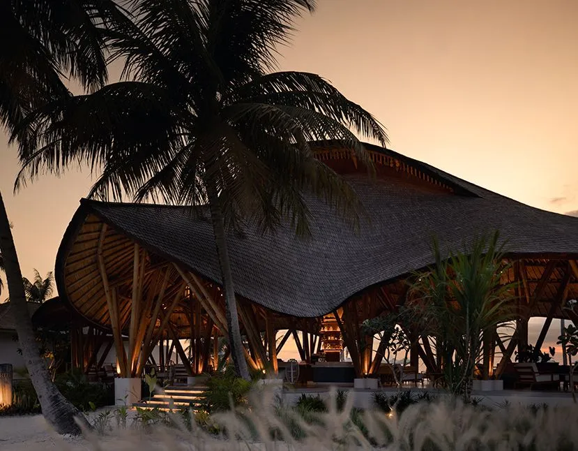 Amrit’s great thatched roof at sunset among the palms, with the beach club’s lights on beneath it.
