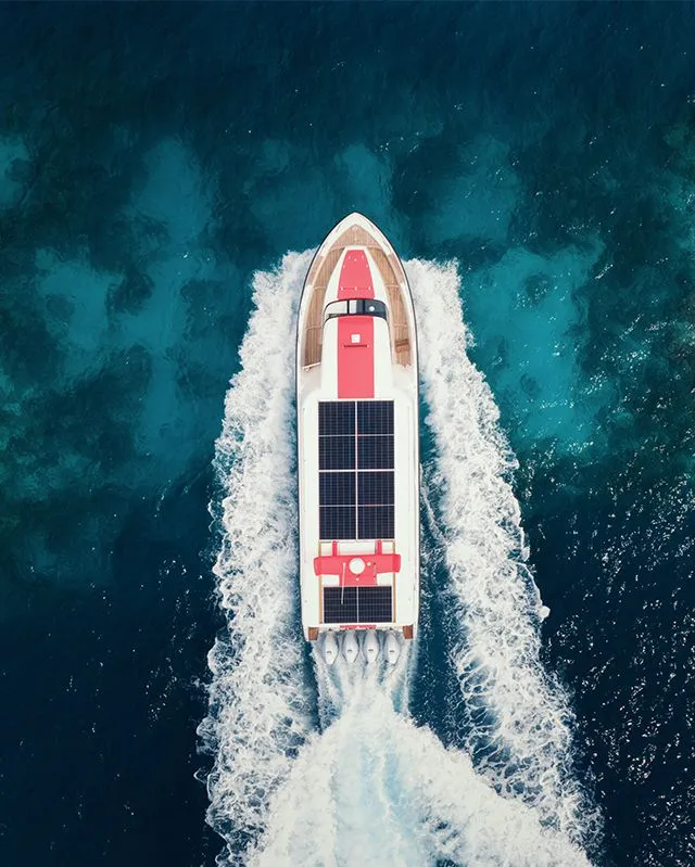 A motor boat seen from above as it speeds across the blue sea, trailing a white wake.