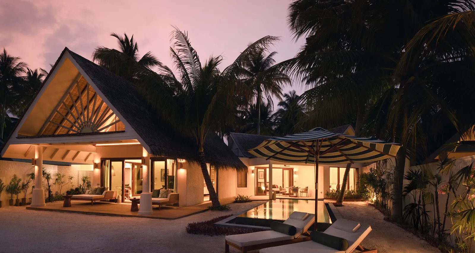 A Family Beach Pool Villa at dusk, its 2 wings lit up and the pool beneath the palms.
