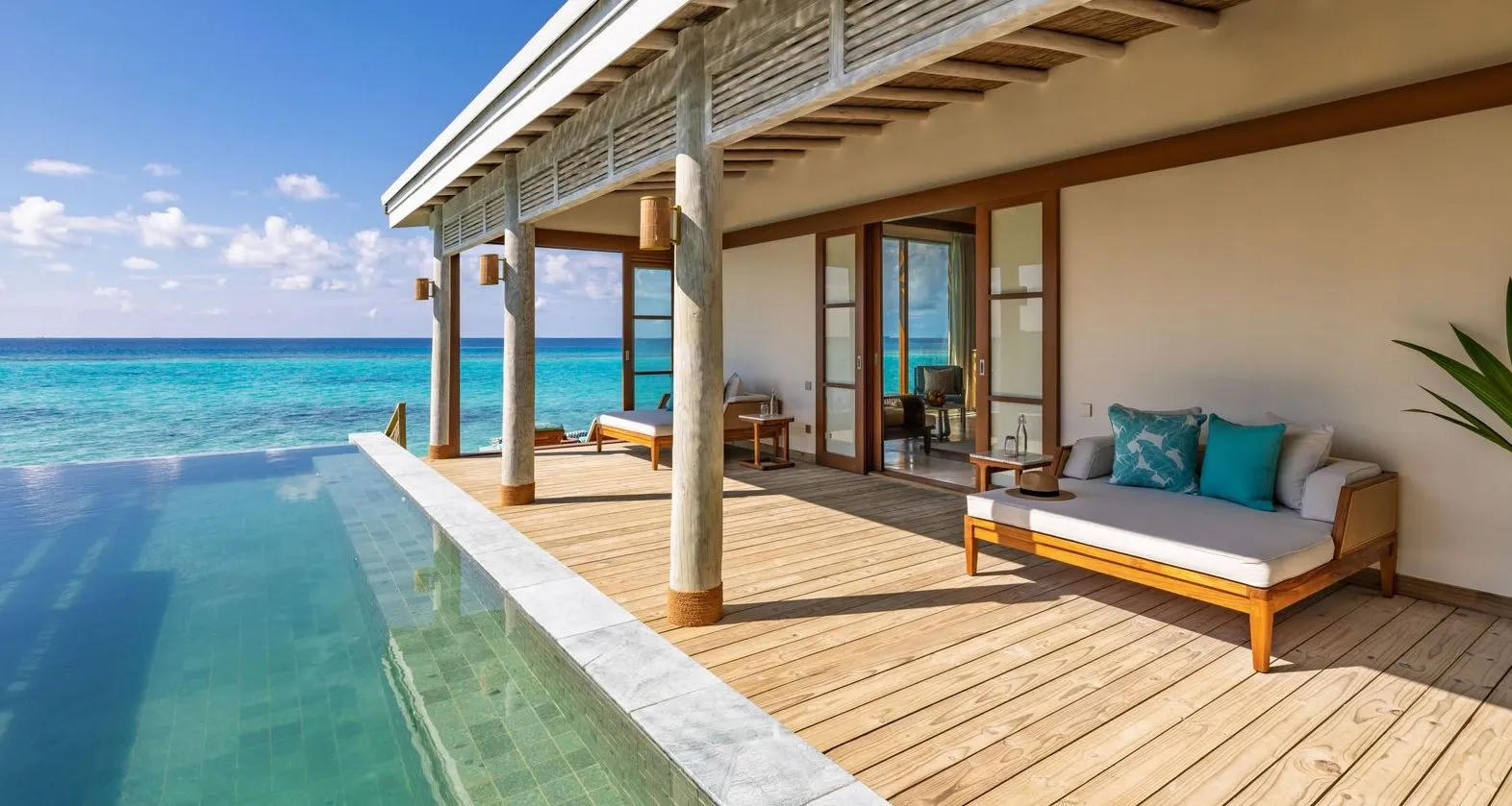 A Water Pool Villa’s timber deck, its infinity pool merging into the lagoon and a daybed under the veranda.