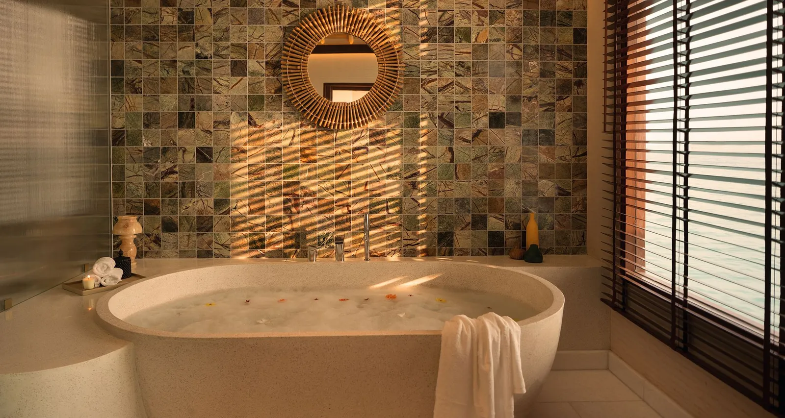 A water villa’s bathroom, with an oval tub, a sunburst mirror and green tiles.