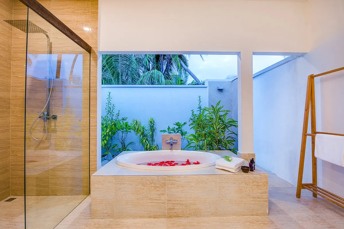 A Lake View Villa’s bathroom, with the sunken bath strewn with petals and the shower behind glass.