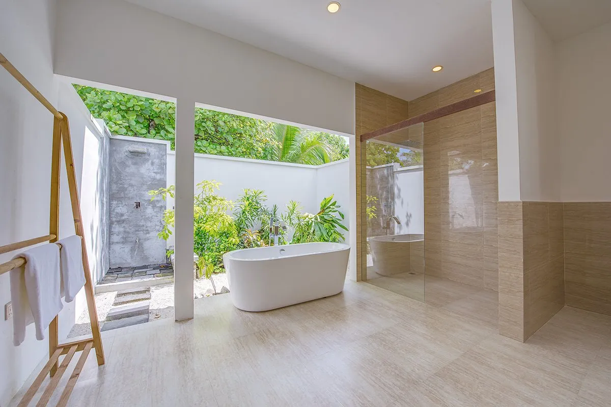 An Ocean View Villa’s open bathroom: the freestanding bath, the shower and the green courtyard behind a low wall.