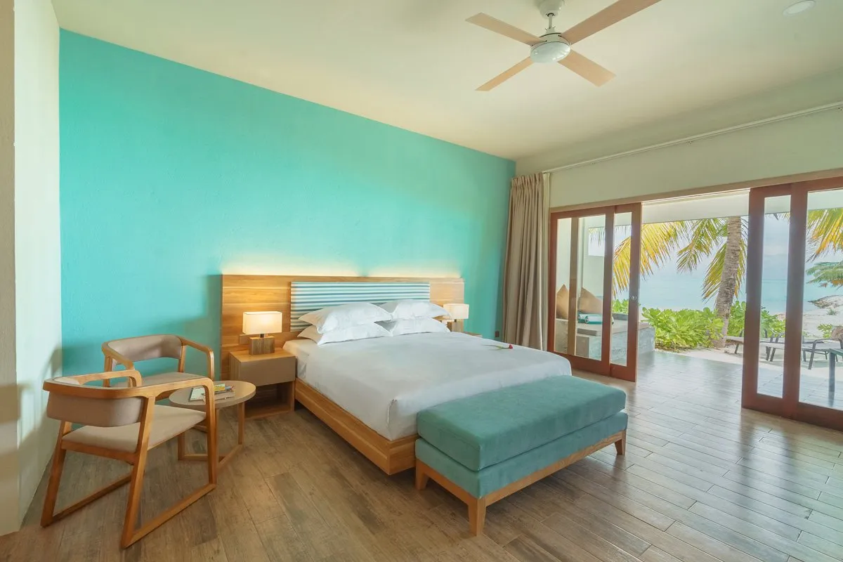 An Ocean View Villa: the bed, the turquoise bench, the ceiling fan and the glass doors open to the garden.