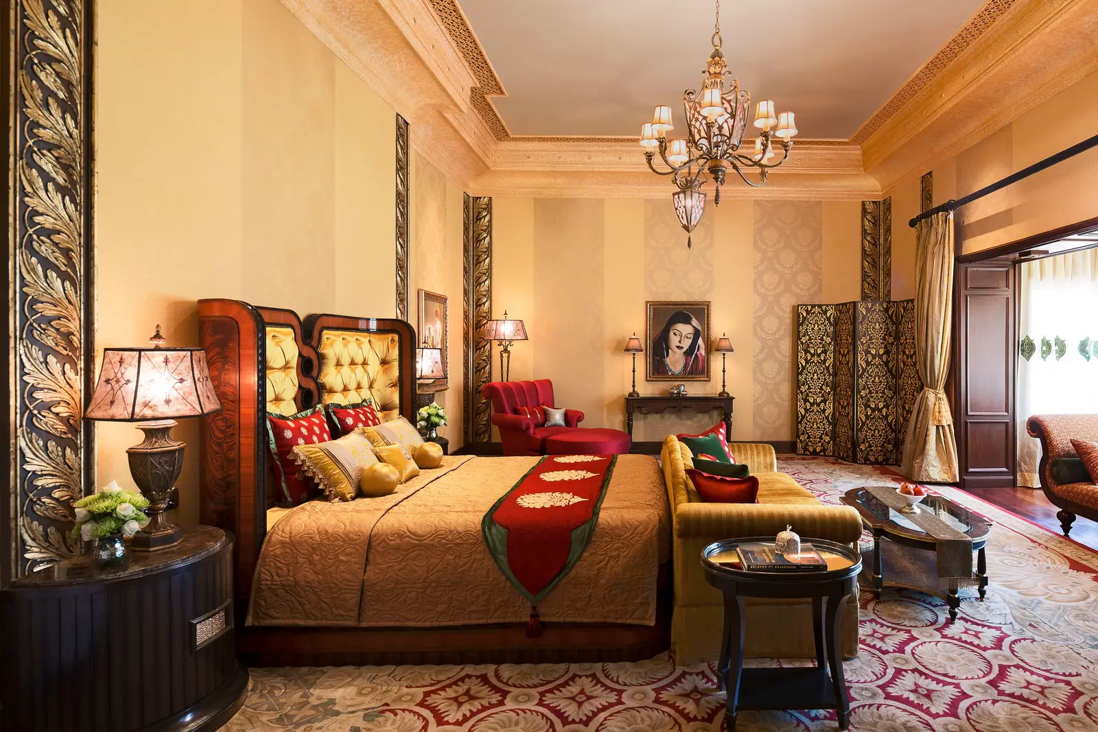 A Grand Royal Suite with a buttoned headboard, chandelier and red armchairs