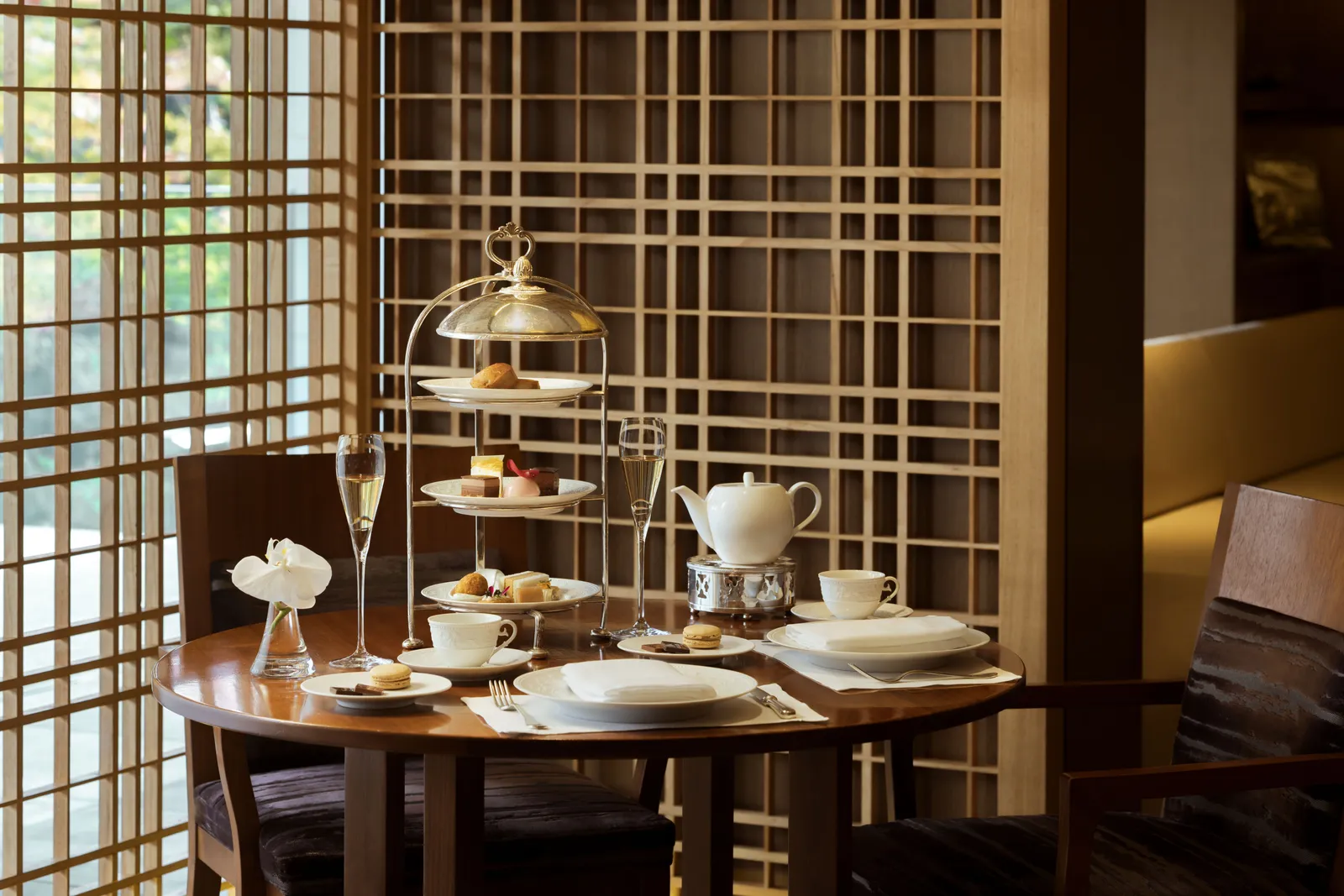 Afternoon tea in The Lobby Lounge: the silver stand of cakes, 2 flutes and a white teapot, behind wooden lattices.