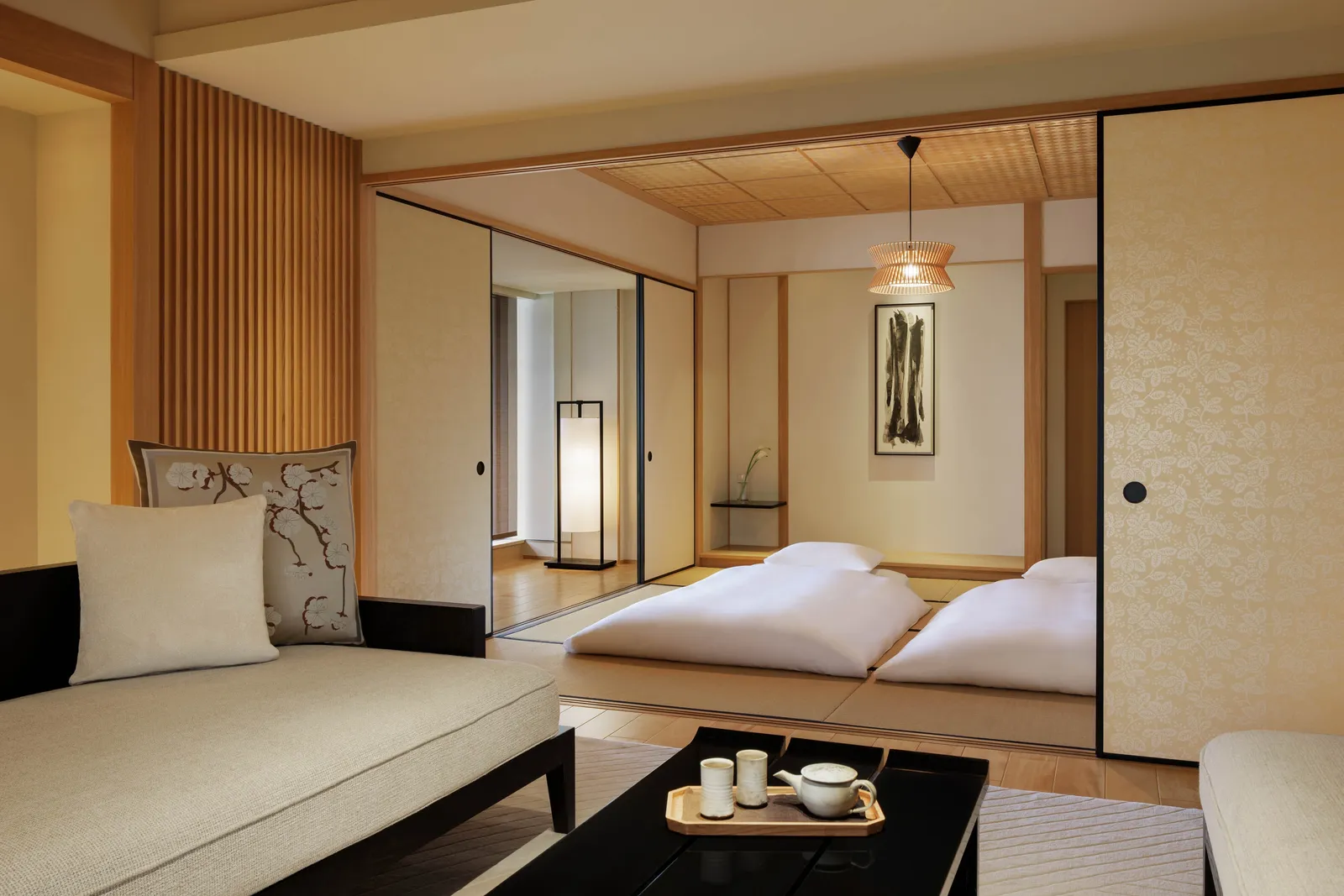 The Corner Suite TATAMI: a low sofa in front and, beyond the open sliding doors, 2 futons on the tatami under a bamboo lamp.