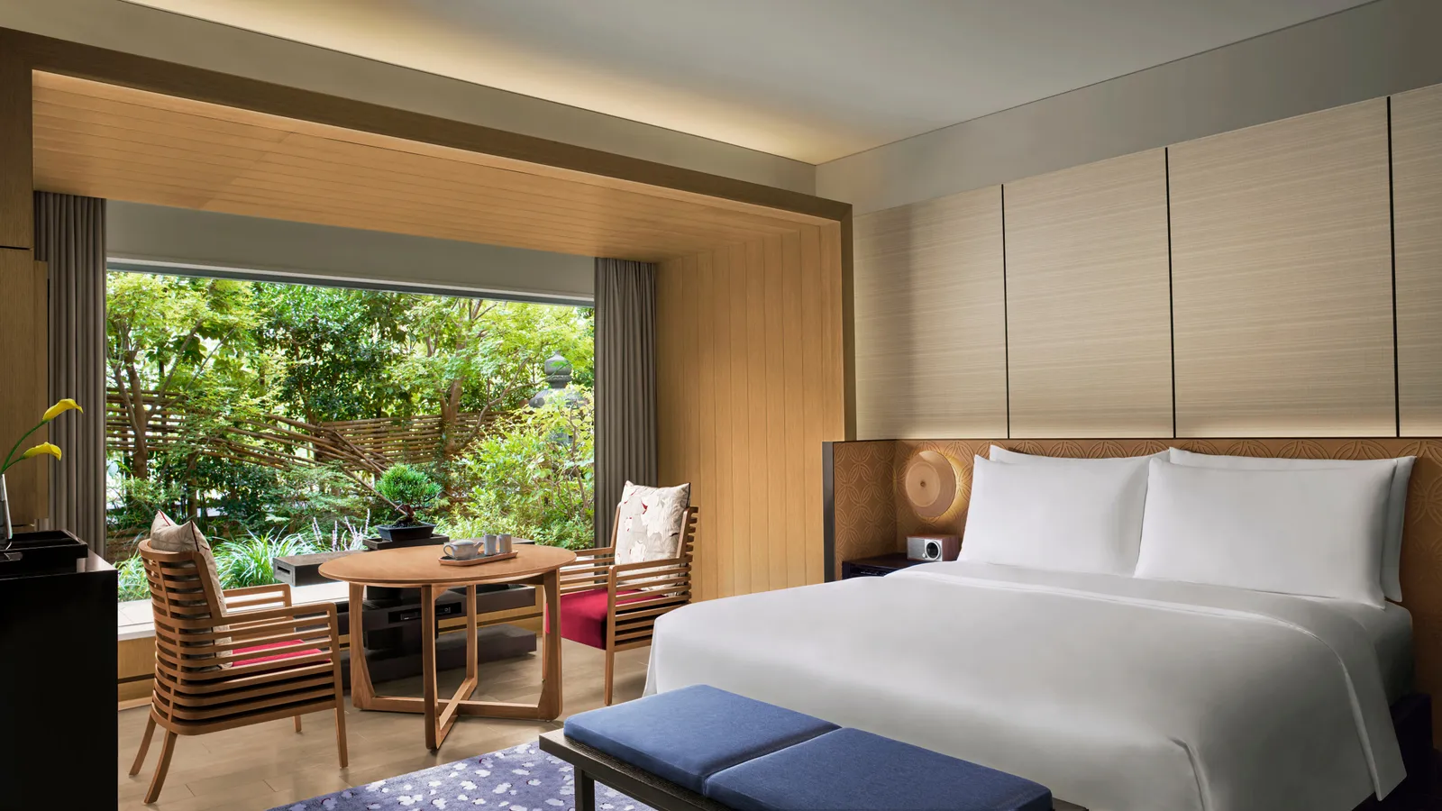 A Deluxe Garden room with its king bed and a wide window onto the garden, maples and shrubs a few steps from the table.
