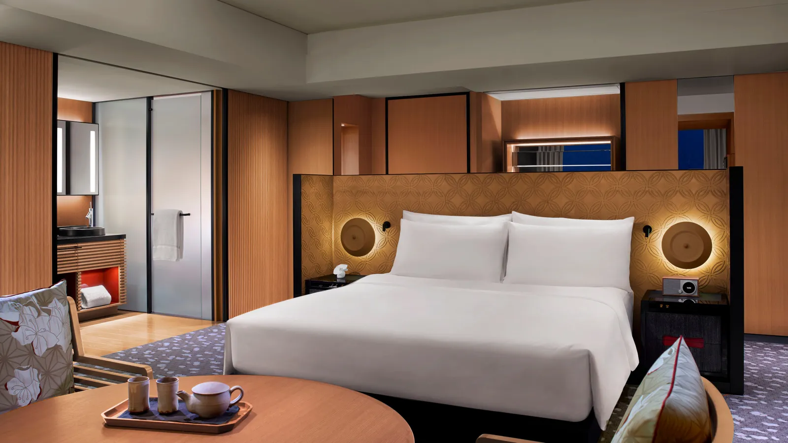 A Deluxe Kyoto room with its king bed against the bathroom wall, a tea set on the table and round lamps either side of the bed.