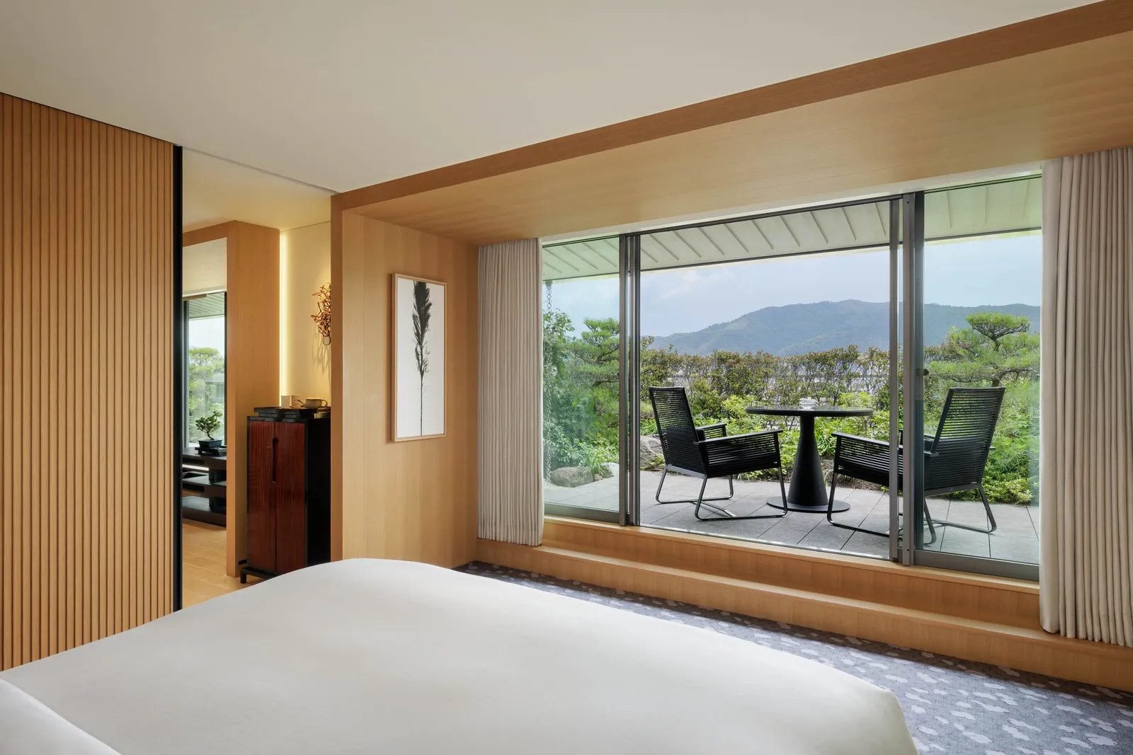 A Garden Terrace Suite bedroom, the bed facing the glass door onto the terrace, 2 chairs and the hills in the distance.