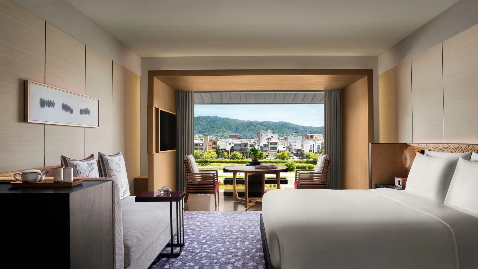A Grand Deluxe Kamogawa room with its king bed, the sofa and the balcony over the river, the houses and the Higashiyama hills opposite.