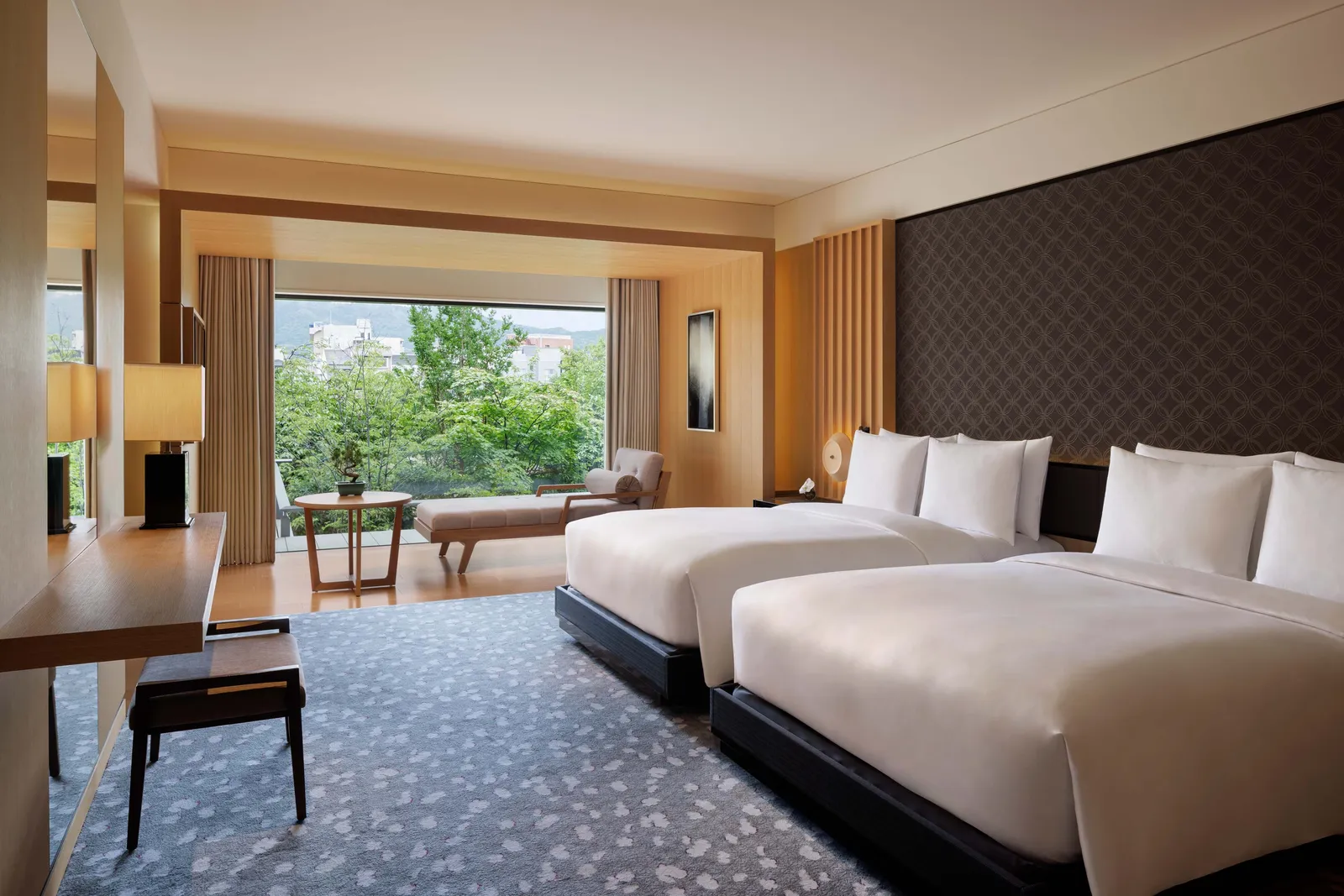 The Suite KAMOGAWA with 2 double beds, a writing desk and the glass wall onto the trees and houses along the river.