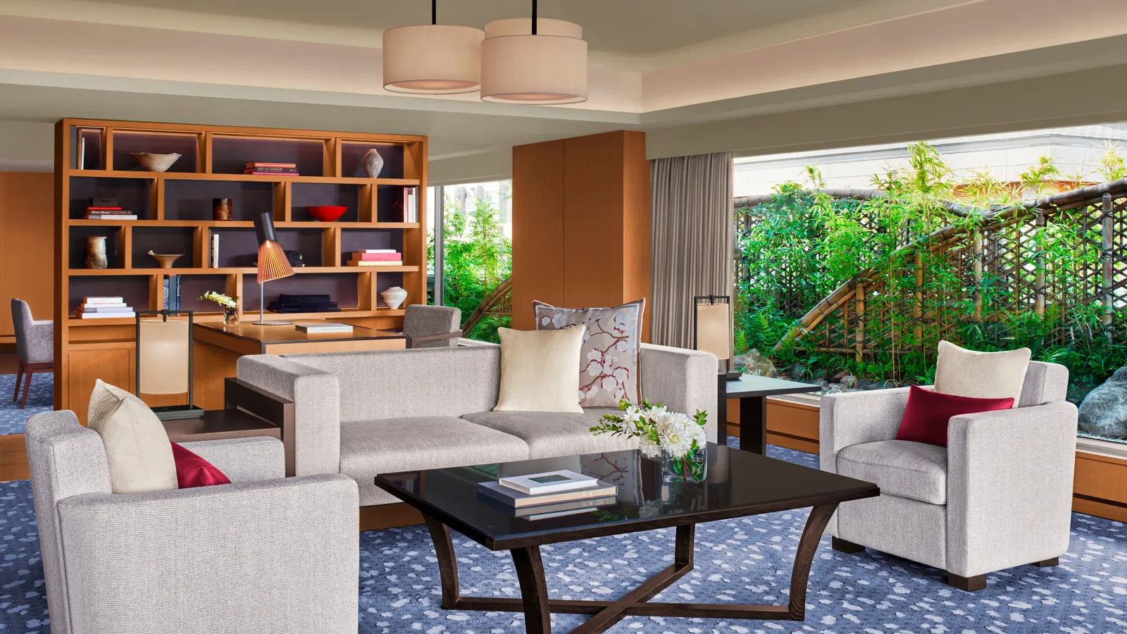 The Suite TSUKIMI living room: sofa and armchairs round a low table, a timber bookcase and the garden beyond the glass.
