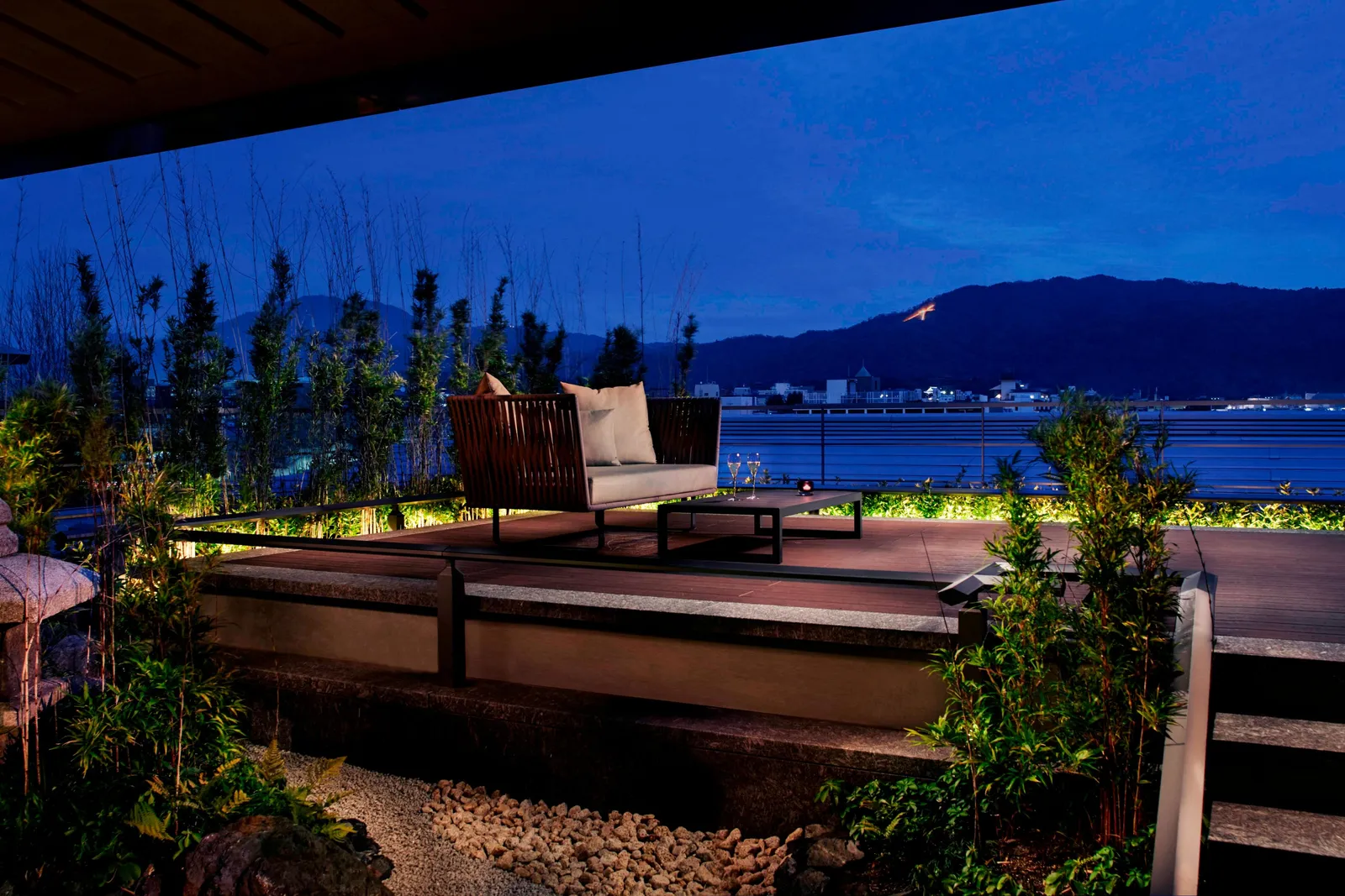 A suite terrace at night: a sofa among lit bamboo and gravel, and on the mountain opposite the Daimonji character ablaze.