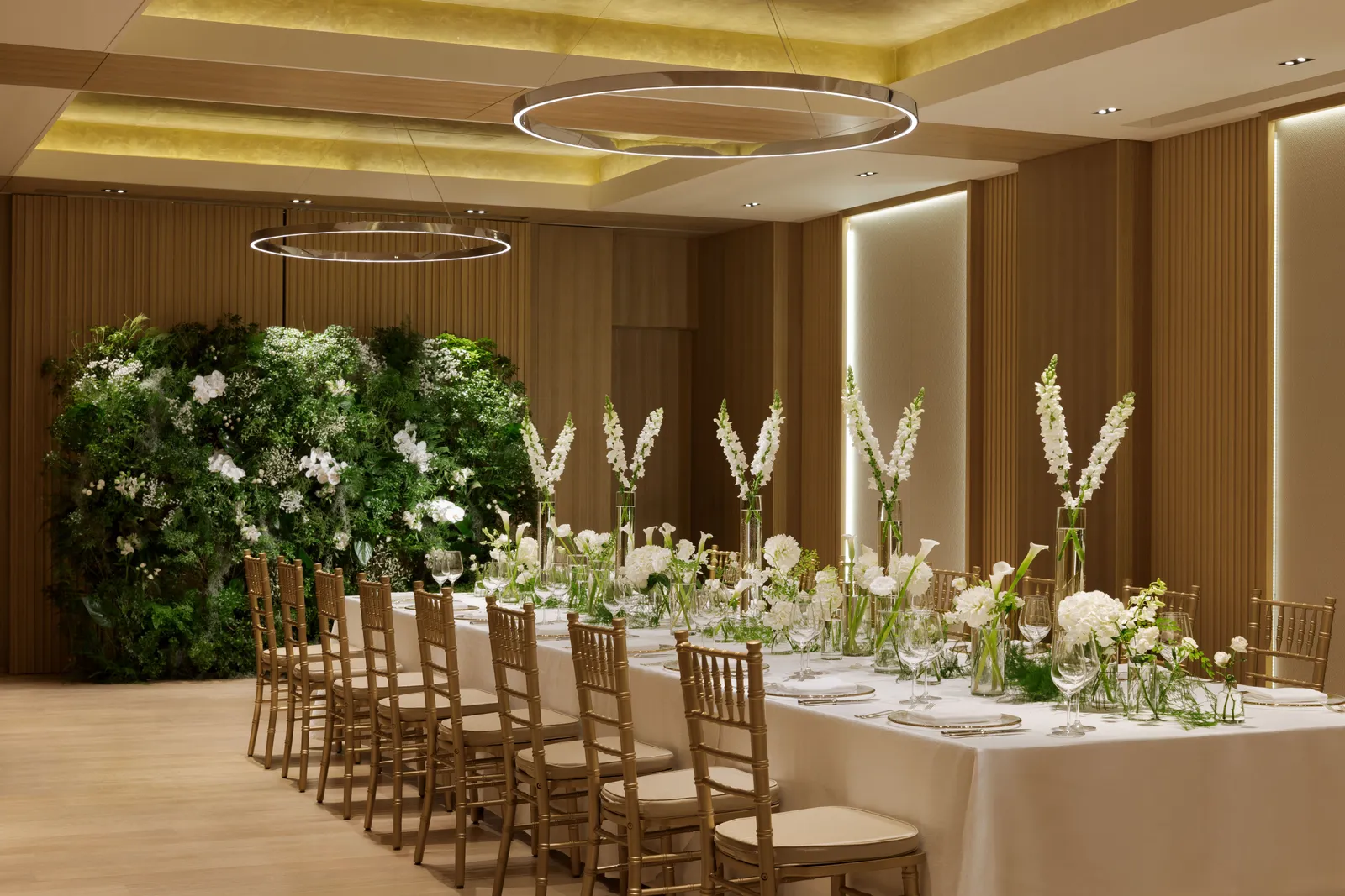 The Kocho room laid for a reception: one long table with tall white flowers, gilt chairs and a wall of greenery.