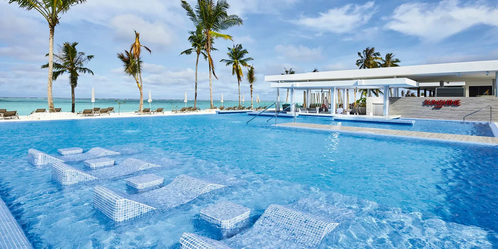 The main pool with its in-water loungers and, behind it, the Sunshine swim-up bar among the palms.