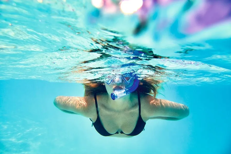 A young woman in a mask swims underwater in the clear lagoon.