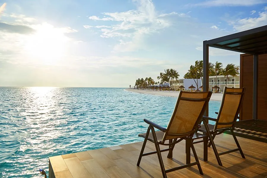 2 chairs on the deck of an overwater Junior Suite, facing the lagoon and a low sun.
